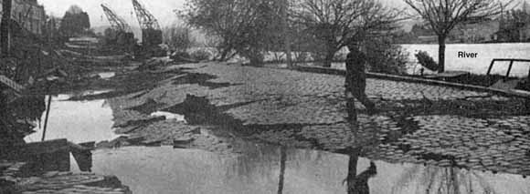 photo of cracked, flooded cobblestone street above river